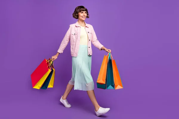 Фотографія повного тіла щасливої молодої жінки ходьба тримає руки магазину продажу сумки ізольовані на фіолетовому кольоровому фоні — стокове фото
