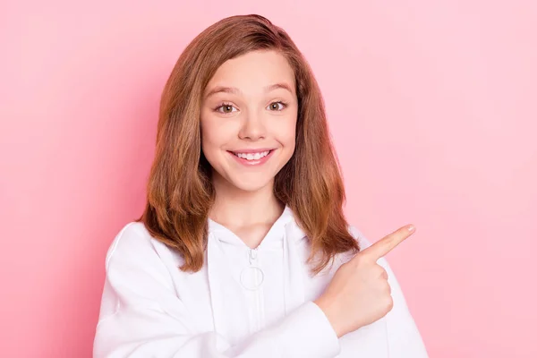 Фотопортрет улыбающаяся девушка в толстовке показывает пустое пространство пальца изолированный пастельно-розовый цвет фона — стоковое фото