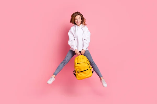 전체 몸길이의 소녀가 학교 가방을 계속 들고 행복하게 격리 된 파스텔 핑크 색 배경을 가지고 뛰어오르다 — 스톡 사진