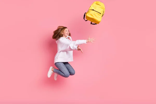 Foto de impressionado funky pequena estudante vestida camisola branca saltando jogando mochila isolado cor de fundo rosa — Fotografia de Stock