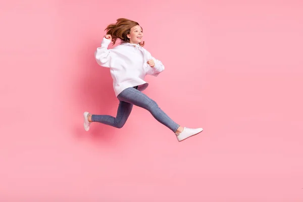 Foto de niña de la escuela brillante dulce usar sudadera con capucha blanca sonriendo saltando alto corriendo buscando espacio vacío aislado color rosa fondo —  Fotos de Stock