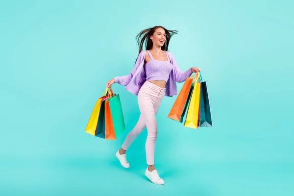 Foto av bedårande söt kvinna klädd lila kläder innehav shoppingväskor promenader ser tomt utrymme isolerad teal färg bakgrund — Stockfoto