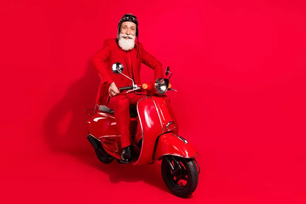 Foto de confiante bonito idade cavalheiro desgaste novo ano traje headwear equitação motocicleta sorrindo isolado cor vermelha fundo — Fotografia de Stock