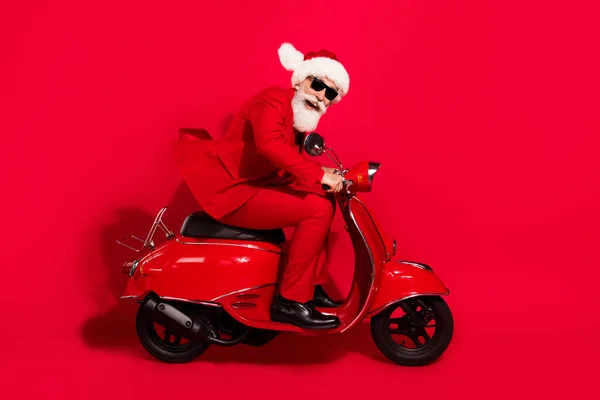 Foto de encantador funky maduro motociclista vestido traje de navidad sombrero sonriendo apresurándose aislado color rojo fondo — Foto de Stock