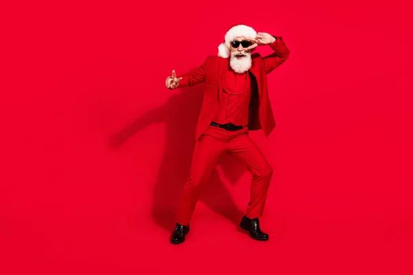 Φωτογραφία του δροσερό αρκετά ώριμος άνθρωπος ντυμένος Χριστούγεννα κοστούμι καπέλο χορό v-σημάδια κάλυψη μάτι απομονωμένο κόκκινο χρώμα φόντο — Φωτογραφία Αρχείου