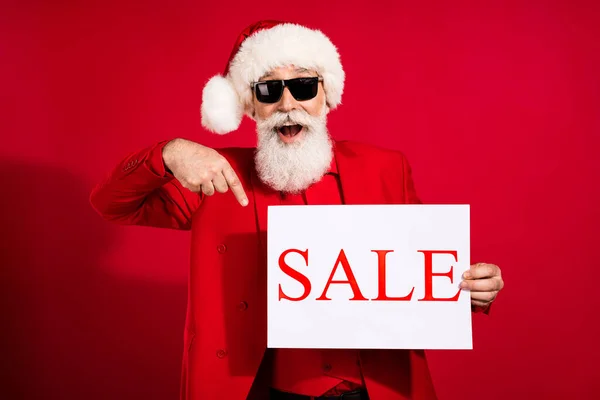 사진의 웃긴 산타 클라우스 직접 손가락 판매 플래카드빨간 배경에 선글라스 x-mas 모자 정장을 착용 — 스톡 사진