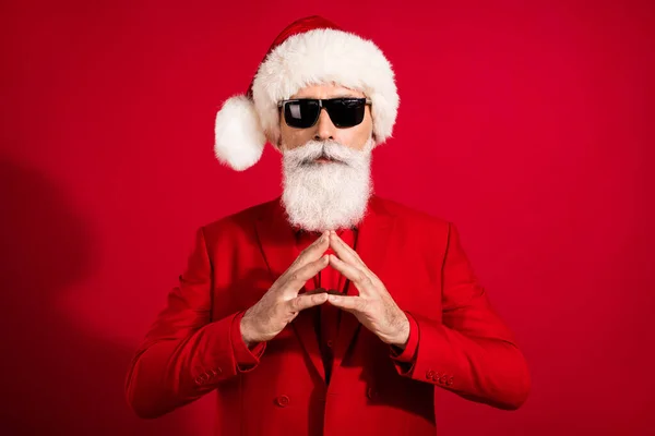 Bild av cool fokuserad Santa claus hålla fingrarna lugna ansikte bära solglasögon x-mas hatt kostym på röd färg bakgrund — Stockfoto