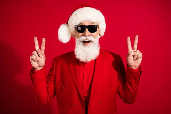 Zdjęcie starego pozytywnego człowieka zrobić palce v-znaków nosić Santa Claus kapelusz izolowany na czerwonym tle koloru — Zdjęcie stockowe