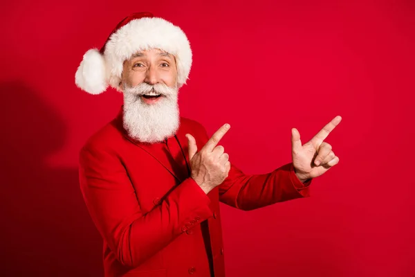 Bild av charmiga söt mogen man klädd jul kostym hatt peka fingrar tomt utrymme isolerad röd färg bakgrund — Stockfoto