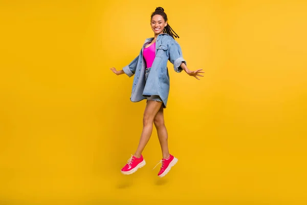 フルサイズプロフィール側の写真の若い黒の女の子幸せな正の笑顔ジャンプアップ歩く旅行隔離された上の黄色の色の背景 — ストック写真