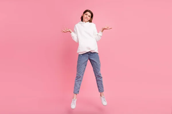 Volledige foto van millennial dame springen schouders dragen hoodie jeans sneakers geïsoleerd op roze achtergrond — Stockfoto