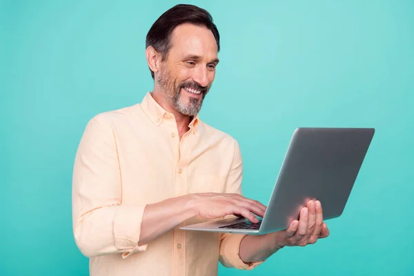 Фото хорошего возраста мужчина работает ноутбук носить персиковую рубашку изолированы на бирюзовом фоне цвета — стоковое фото