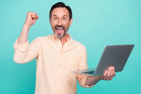 손으로 컴퓨터를 들고 청록색 배경에 고립된 복숭아 셔츠를 입고 있는 놀란 나이든 남자의 사진 — 스톡 사진