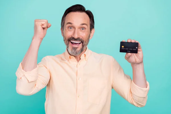 Foto van gelukkig gek glimlachen man verhogen vuist in overwinning triomf houden credit debit card geïsoleerd op turquoise kleur achtergrond — Stockfoto