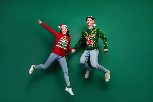 Foto de alegre x-mas pareja salto fiesta desgaste santa sombrero feo suéter aislado color verde fondo —  Fotos de Stock