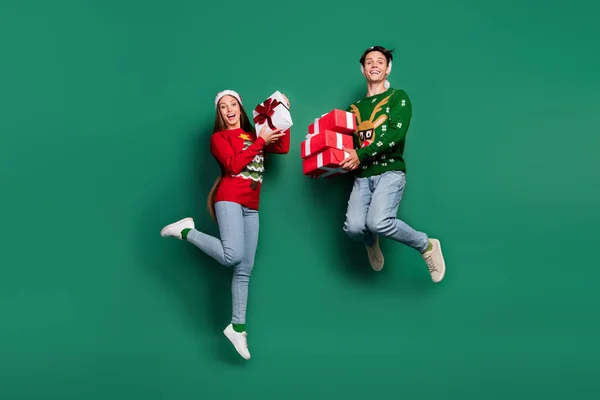 Foto von verrückten sorglosen Paar halten Geschenk-Boxen springen tragen hässlichen Pullover isoliert grüne Farbe Hintergrund — Stockfoto