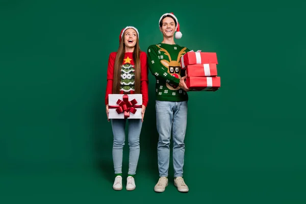 兴奋的梦想成真的夫妻拿着堆积如山的礼物享受圣诞派对穿着丑陋的毛衣与世隔绝的绿色背景 — 图库照片