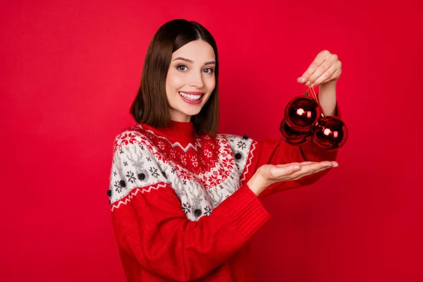 Фото милої красивої молодої жінки, одягненої в принт пуловер, що тримає новорічні прикраси ізольований червоний колір фону — стокове фото