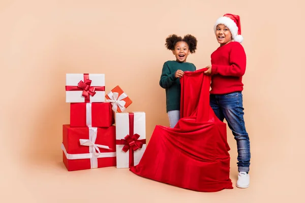 Photo of two people kids prepare unpack presents sack wear x-mas hat jumper isolated beige color background — Stock Photo, Image