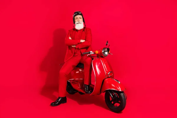 Foto van schattige ernstige leeftijd heer dragen nieuwjaar kostuum hoofddeksel rijden motorfiets armen gekruist geïsoleerde rode kleur achtergrond — Stockfoto