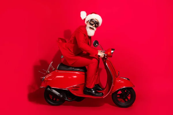 Photo of cute impressed age gentleman wear new year costume spectacles riding motorcycle smiling isolated red color background — Stock Photo, Image