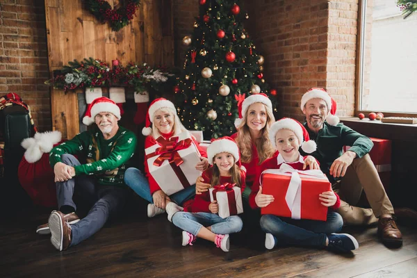 Retrato de família alegre atraente usando chapéus segurando presentes de dezembro sentado na árvore do assoalho em casa casa casa loft dentro de casa — Fotografia de Stock