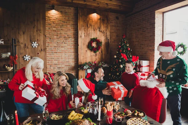 Mutlu aile portresi. Masada oturan mutlu aile resmi. Kırmızı başlık takmış, kış tatillerinde Noel hediyesi kutuları veriyor. — Stok fotoğraf