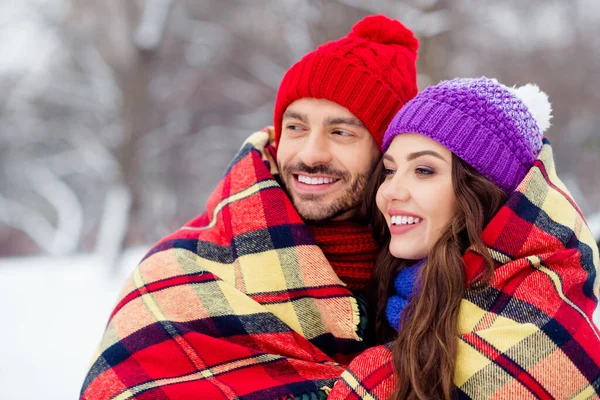 Foto av vackra söta äktenskap par bära vindjackor leende kramar täcker rutig filt promenader snöig utanför park — Stockfoto