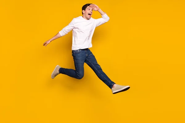 Foto de perfil de comprimento total de impressionado morena jovem salto olhar desgaste camisa jeans tênis isolado no fundo amarelo — Fotografia de Stock