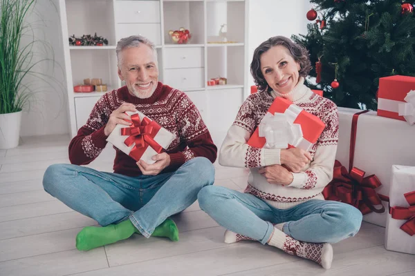 Foto av söt charmig ålder par klädd tryck pullovers sittande ben korsade omfamna gåvor leende inomhus rum hem hus — Stockfoto