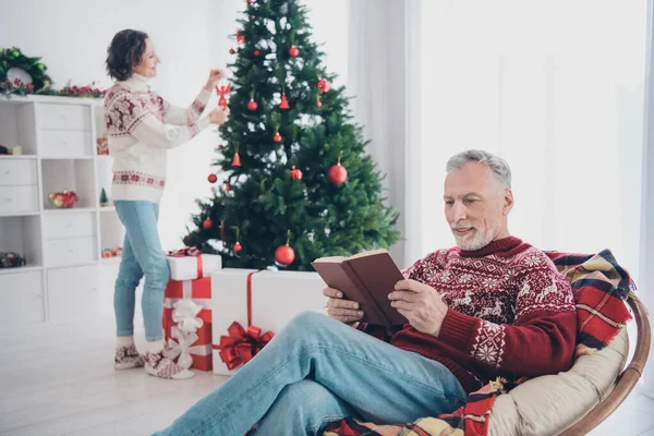 Zdjęcie miłej pary staruszka powiesić zabawki człowiek czytać książki nosić sweter dżinsy skarpety w domu — Zdjęcie stockowe