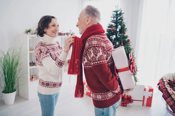 Bild av skinande charmig ålder par klädd tryck pullovers presentera gåvor leende inomhus rum hem hus — Stockfoto