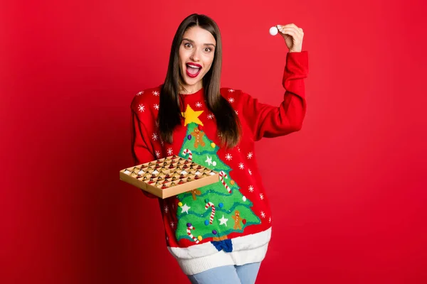 Photo de brillante excitante jeune femme habillée laid pull souriant tenant décorations de Noël isolé fond de couleur rouge — Photo