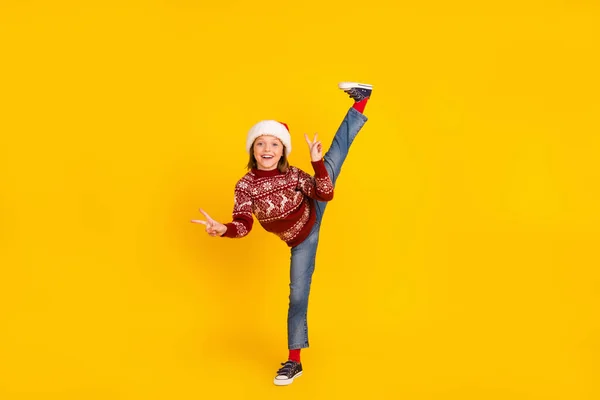 Pleine longueur photo de petite fille gaie sauter jusqu'à flexible lever jambe Noël isolé sur fond de couleur jaune — Photo