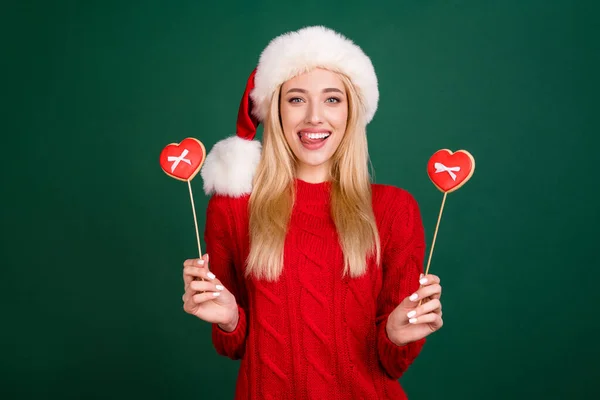 Foto de bonita jovem mulher vestida de malha pulôver língua lambendo lábios segurando cookies isolado cor verde fundo — Fotografia de Stock