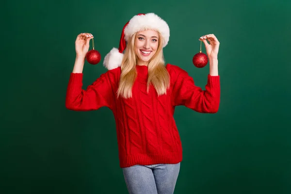 Фото блискучої чарівної молодої леді носить червоний светр головний убір посміхаючись тримає кульки ізольований зелений колір фону — стокове фото