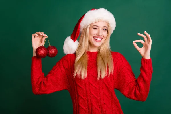 Foto retrato mulher loira em santa chapéu sorrindo pendurado bolas na árvore de xmas mostrando bem isolado fundo cor verde — Fotografia de Stock