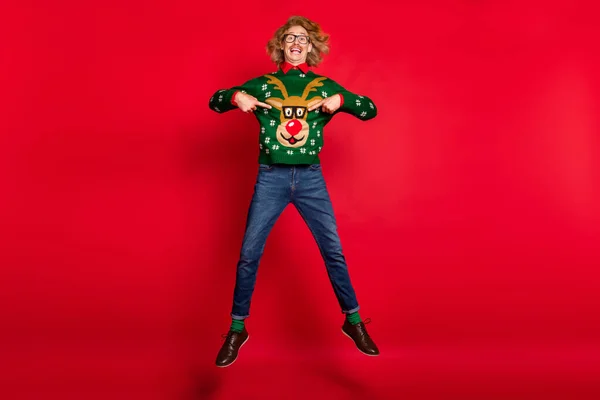 Foto tampan funky pemuda mengenakan sweater hijau melompat menunjuk jari-jari sendiri tersenyum terisolasi warna latar belakang merah — Stok Foto