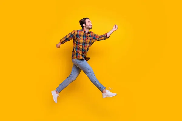 Foto de perfil de longitud completa de divertidas brunet millennial guy run wear shirt jeans sneakers aisladas sobre fondo amarillo —  Fotos de Stock