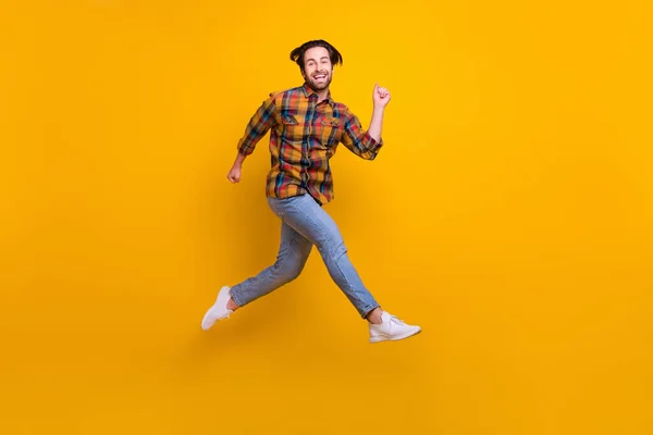 Фотографія повного тіла божевільного брюнетки молодий хлопець біжить носити сорочки джинси кросівки ізольовані на жовтому фоні — стокове фото