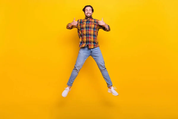Pleine longueur photo de cool brunet millennial guy saut montrer pouce vers le haut porter chemise jeans baskets isolé sur fond jaune — Photo