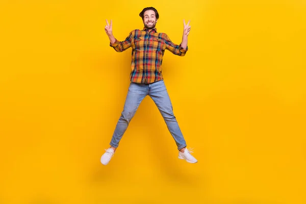 Full body photo of crazy brunet young guy jump show v-sign wear shirt jeans sneakers isolated on yellow background — Stock Photo, Image