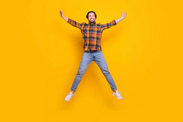 フルサイズの写真の甘いブルネットミレニアル男ジャンプ着用シャツジーンズスニーカー隔離された黄色の背景 — ストック写真