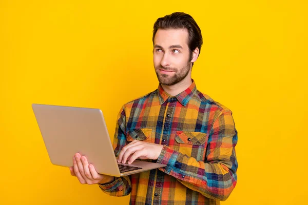Zdjęcie dość przemyślany młody człowiek nosić koszulę w kratę uśmiechnięty wpisując nowoczesne urządzenie patrząc puste miejsce odizolowany żółty kolor tło — Zdjęcie stockowe