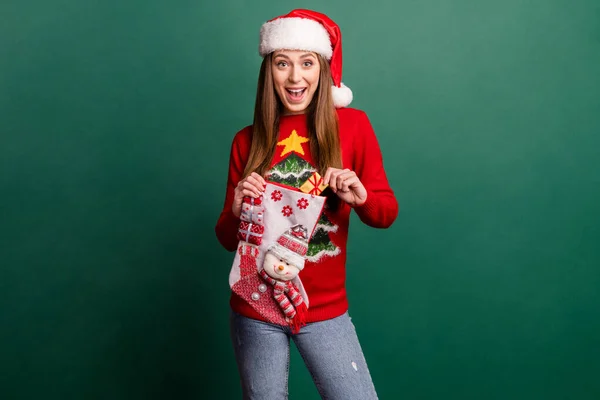 Фото дивовижно збудженої щасливої молодої жінки посмішка тримає руку різдвяної шкарпетки ізольовано на фоні зеленого кольору — стокове фото
