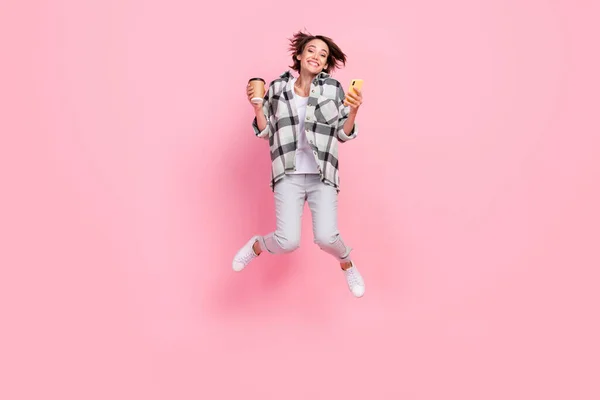 Teljes hosszúságú fotó vicces Y-generációs barna hölgy ugrás hold kávé telefon kopás ing nadrág cipő elszigetelt rózsaszín háttér — Stock Fotó