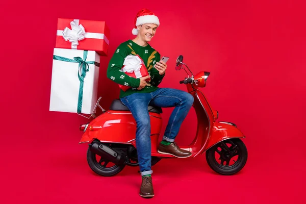 Ganzkörpergröße Foto Mann lächelnden Kerl Sitzen auf dem Fahrrad mit Smartphone halten Gegenwart isoliert lebendige rote Farbe Hintergrund — Stockfoto