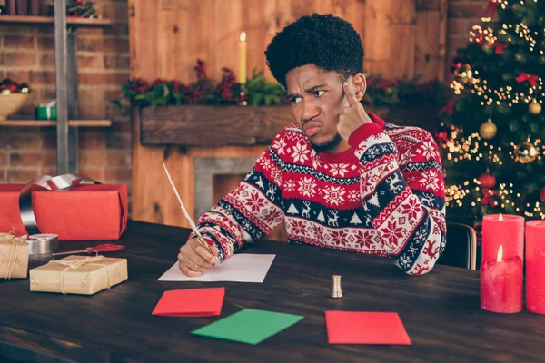 Foto von charmanten zweifelhaften dunkelhäutigen Kerl gekleidet Print-Pullover Schreiben Neujahrswünsche drinnen Haus Home Room — Stockfoto