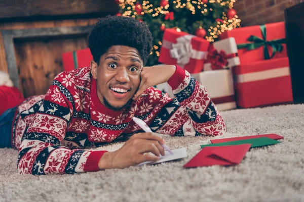 Фото довольно взволнованный темная кожа человек носить красный свитер написания рождественские поздравления улыбаясь в помещении домашний дом — стоковое фото