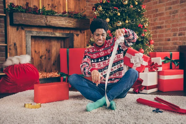 Фото милой довольно темной кожи мужчина носить красный свитер украшая Рождество представляет улыбаясь в помещении домашний дом — стоковое фото